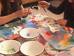 Children painting around a table full set with bowls and paint.